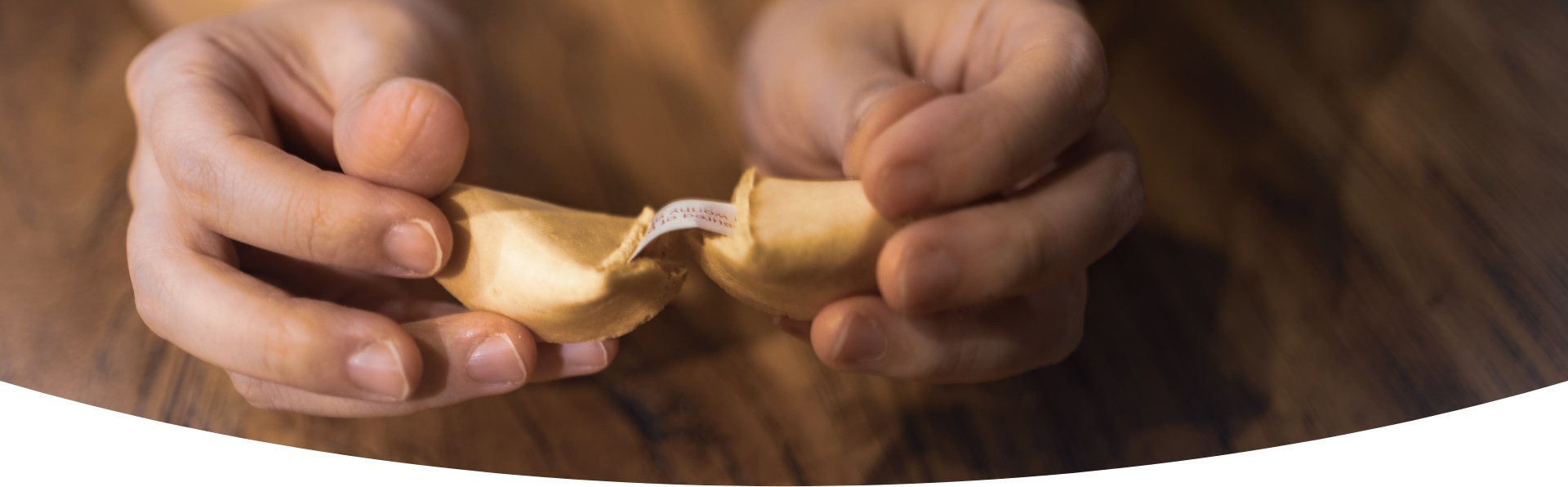 A man opens a fortune cookie. Only his hands and the fortune cookie can be seen.